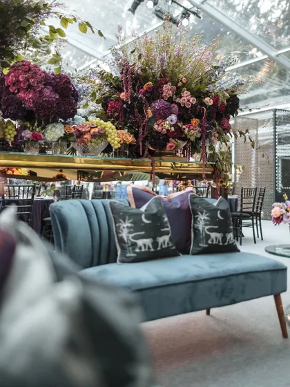 A plush velvet lounge sofa with custom-printed pillows, part of a luxurious Sangeet in the English countryside. Every detail, down to the soft furnishings, is curated to fit the theme.
