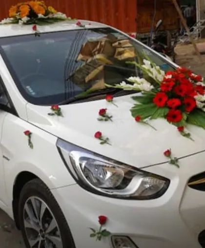 A simple and clean wedding car decoration on a Hyundai Verna. It features a central bouquet of red and white flowers with single roses placed on the bonnet.