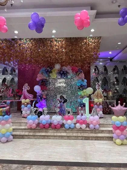 A magical Disney Princess theme for Kridha's first birthday. The stage is decorated with a shimmer wall, a pastel balloon arch, and cutouts of different princesses.
