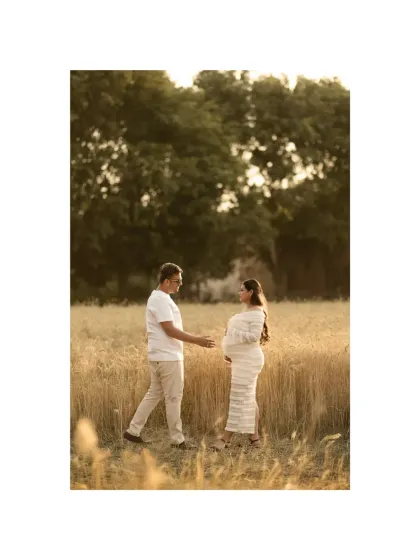 A candid moment in a golden wheat field. The father-to-be reaches for his partner's hand, a gesture of support and love as they stand in a field symbolizing growth and life.