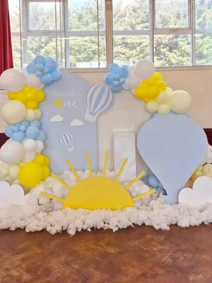 A bright and cheerful hot air balloon theme with a large sun cutout and fluffy cotton clouds on the floor.