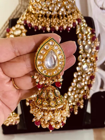 A close-up of a large Kundan jhumka earring, part of a full bridal set. The red and green Meenakari work on the earring top adds a touch of traditional color.