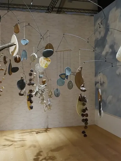 The mobile sculpture from the 'Feel More' installation, seen against a backdrop of a painted sky. The piece is a delicate balance of natural and crafted elements, designed to evoke wonder.