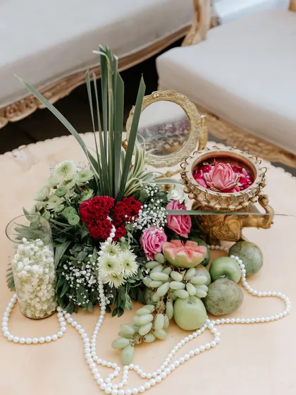This traditional centerpiece combines fresh flowers, fruits, and pearls with a vintage-style brass mirror, creating a look of classic elegance.