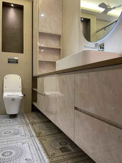 We used large, glossy marble-finish laminate for the vanity in this bathroom, paired with beautiful patterned floor tiles. The design includes a mix of open and closed storage for functionality.