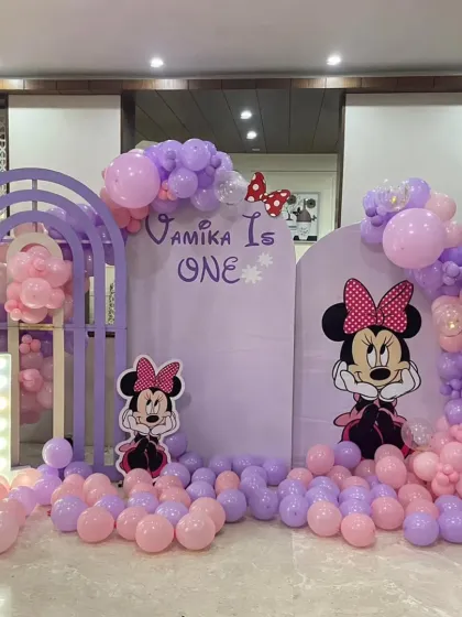 I bring classic characters to life, like this Minnie Mouse first birthday party. The setup includes custom arched backdrops in a lovely lavender and pink palette, character cutouts, and a light-up marquee number.