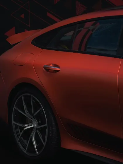 A close-up on the rear quarter panel and door handle of a matte orange Mercedes-AMG. The lighting is used to accentuate the car's muscular curves and unique paint finish.