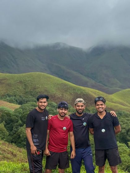 Four friends posing together against the misty green hills of Kudremukha.