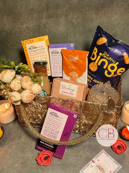 Celebrating the festival of light with heartfelt surprises. This golden wire basket is filled with healthy chocolates from The Whole Truth, Binge puffs, Starbucks coffee, and a diamond jar candle.