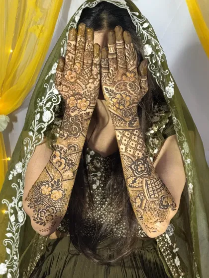The bride's hands frame her face, showcasing the beautiful and detailed floral and paisley patterns of her Dubai-style mehendi.