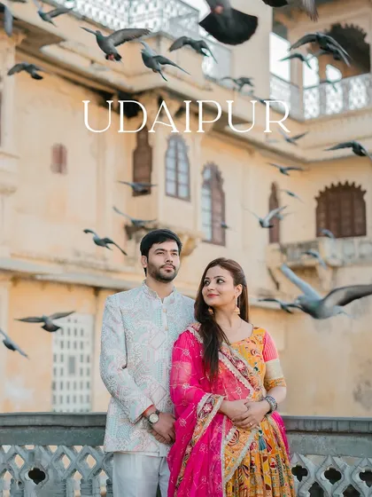 A wide shot capturing the couple amidst a flock of pigeons with "Udaipur" text, highlighting the destination and the dynamic environment.