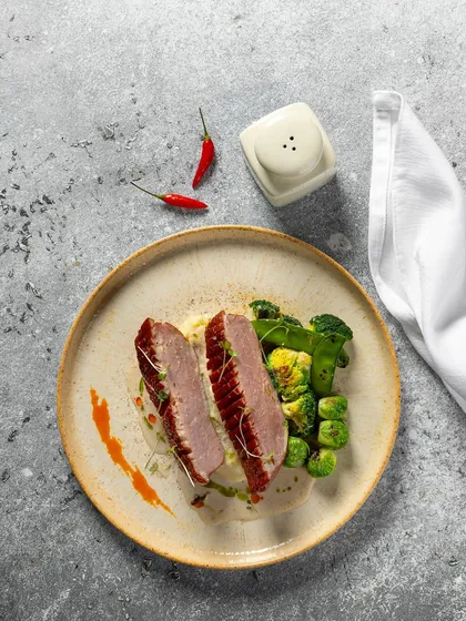 Sliced grilled meat with brussels sprouts and broccoli, shot for Novotel New Delhi. The minimalist plating on a textured plate gives this dish a modern, gourmet feel.