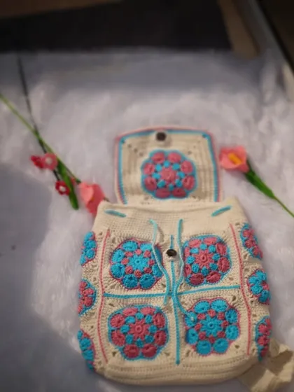 A styled shot of the custom backpack, showing its beautiful design and structure. It's laid on a soft surface with flowers, highlighting its artistic quality.