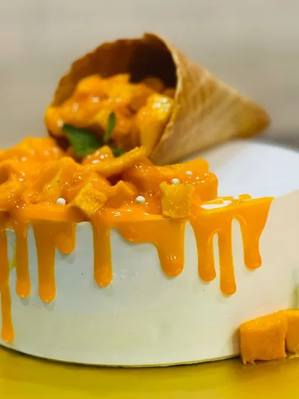 A beautiful Fresh Mango Cake with a gravity-defying cone spilling out fresh mango pieces. This is one of our most popular seasonal cakes, celebrating the king of fruits.