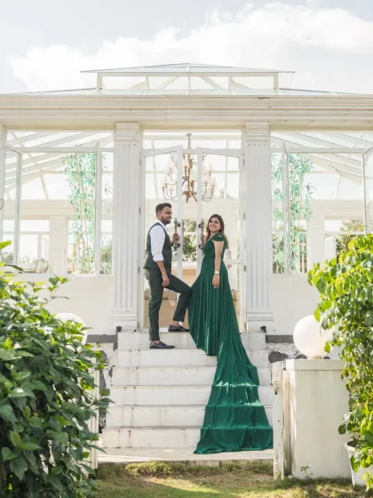 A grand pose on the steps of a white conservatory. The bride's emerald green gown with its long train cascades down the stairs, creating a visually stunning and regal image.