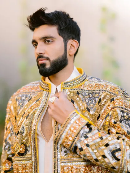 A handsome portrait of the groom in his intricately detailed golden sherwani. The soft, natural light highlights his sharp features and confident presence.