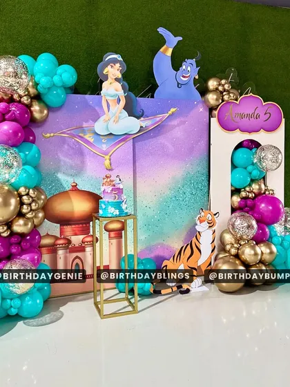 A magical Aladdin-themed party for a fifth birthday. The setup features a purple and teal backdrop of Agrabah, cutouts of Jasmine, Genie, and Rajah, and gold and glitter balloons.