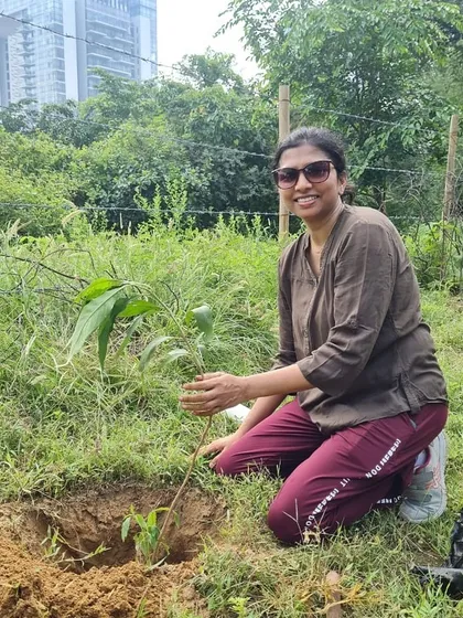A volunteer from NatWest proudly kneels by the sapling she just planted. Each tree contributes to restoring soil health and boosting groundwater levels at the site.