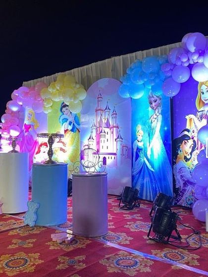 A full view of an outdoor princess party stage, with multiple princess backdrops and a large light-up number '1'.