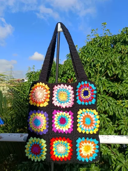 The rainbow granny square tote bag hanging against a beautiful outdoor background, showing off its bright colors.