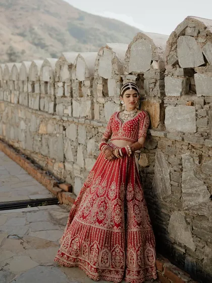 A stunning portrait of the bride in her red wedding lehenga, posing against the ancient stone walls of the destination venue.