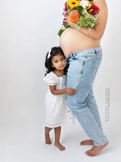 A quiet moment of connection as a little girl rests her head against her mother's pregnant belly. A simple, beautiful portrait of the wait.