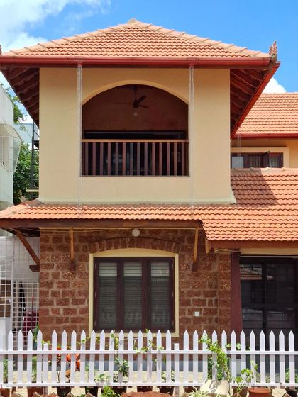 The exterior of the Basavanagudi house, featuring a balcony that overlooks the garden. The combination of exposed laterite stone on the ground floor and smooth lime plaster on the first floor creates a pleasing textural contrast.