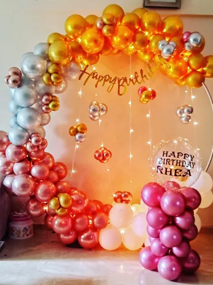 An intimate and magical birthday ring setup for Rhea. This home decoration features a balloon hoop adorned with metallic pink and gold balloons, intertwined with fairy lights for a warm, sparkling effect.