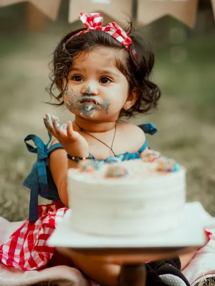 The pure, messy joy of a first birthday cake smash. This close-up shot captures the delightful details, from the frosting on her face to the wonder in her eyes.