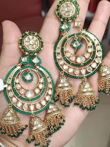 A pair of large, circular kundan earrings with three jhumkis hanging below. The green beads add a pop of color.