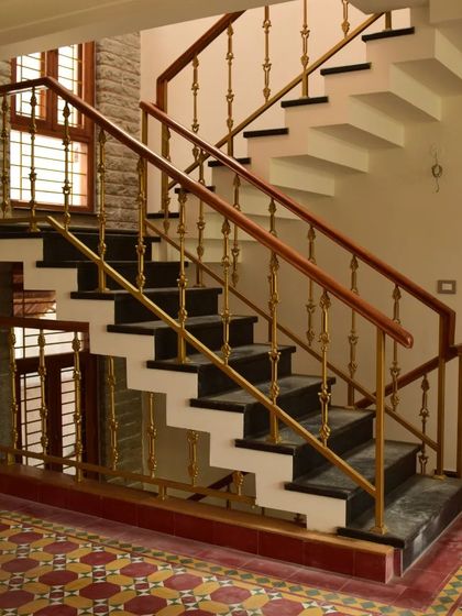 A staircase with black granite steps and ornate brass railings, set against a backdrop of patterned Athangudi floor tiles.