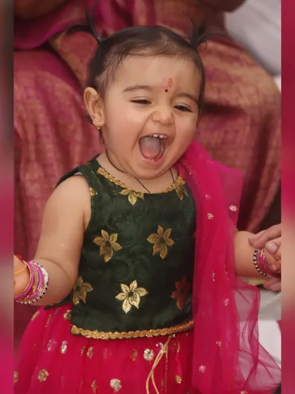 The pure, unfiltered joy of childhood. This candid close-up captures a baby girl's infectious laughter during a family function, showcasing her adorable ethnic lehenga.