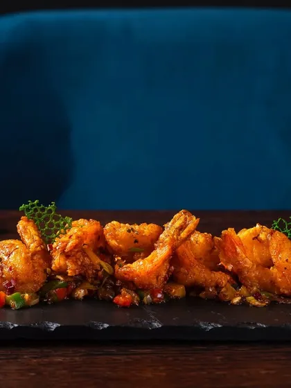 Double-fried prawns in XO and Sichuan sauce, elegantly plated on a black slate platter. The dark background makes the vibrant colors of the dish pop.