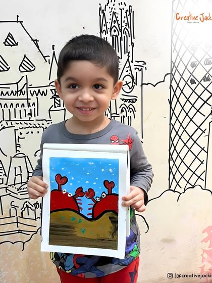 A little boy proudly shows off his painting of two red crabs on a beach, a cute and creative piece from our kids' art session.