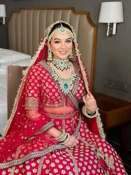 A radiant bride in a classic red and green lehenga. The makeup is timeless, with defined eyes and a warm lip color that complements the rich tones of her outfit.