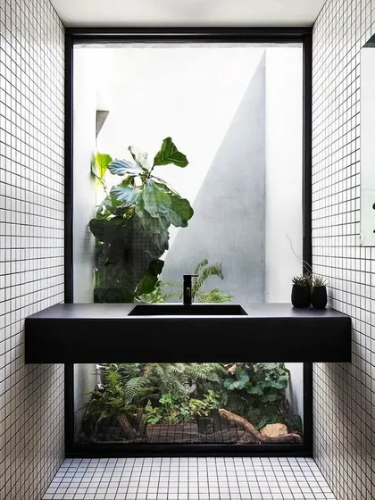We believe in connecting interiors with nature. This powder room concept, with its large window overlooking a private green courtyard, turns a simple utility space into a serene experience. The minimalist black vanity contrasts beautifully with the organic view.