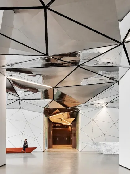 A view from the side of the reception desk, showing how the geometric forms of the desk, seating, and ceiling create a cohesive and immersive architectural language throughout the lobby.