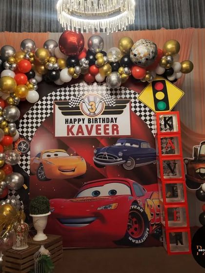 The main stage for the 'Cars' themed 3rd birthday, with a large backdrop, balloon arch, and traffic light prop.