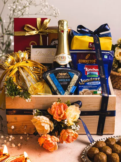 The signature 'UTSAV' hamper is the epitome of luxurious welcome gifting for wedding guests. This gourmet gift basket, presented in a keepsake wooden crate, features sparkling wine, Danish blue cheese, premium chocolates, and assorted snacks, all beautifully arranged with floral accents.