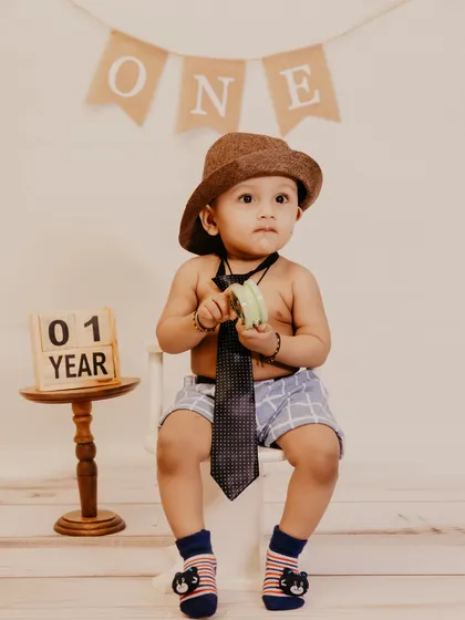 A first birthday studio portrait featuring a '01 YEAR' block prop next to the charmingly dressed baby boy.