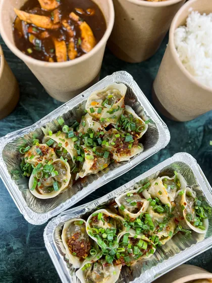 Pan-fried gyoza, drizzled with chili oil and spring onions, ready for delivery. These are perfect for an Asian-themed party at home.