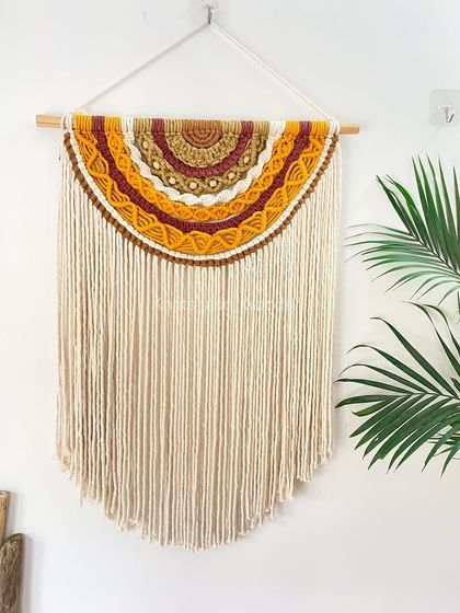 A full view of the half-moon wall hanging, showing how its long, flowing fringe adds a sense of calm and elegance. It hangs beautifully on a natural wood dowel and brings a touch of sunset warmth indoors.