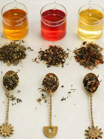 A top-down shot displaying various loose-leaf tea blends in spoons next to their brewed counterparts, showing the beautiful colors of the infusions.