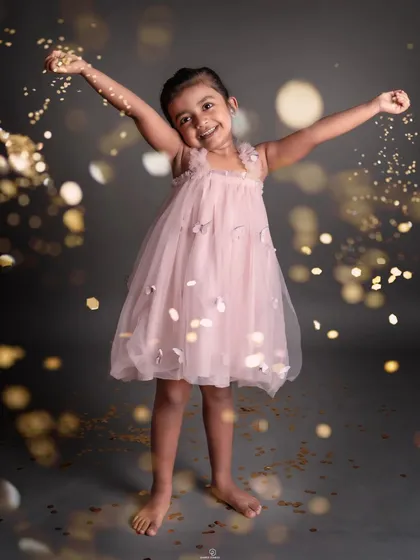 A moment of pure, carefree joy. This little girl's happiness is infectious as she plays with golden confetti in her beautiful pink dress.