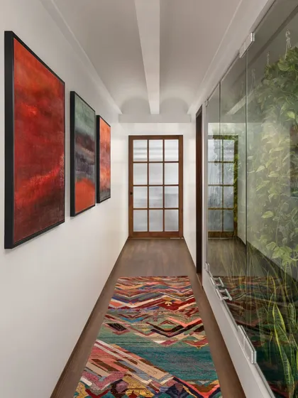 Passageways in our designs are more than just corridors; they are curated experiences. Here, a gallery wall of contemporary Indian art is set against a backdrop of warm, recycled Burma teak flooring, with a glass wall offering a glimpse into a light-filled interior courtyard.