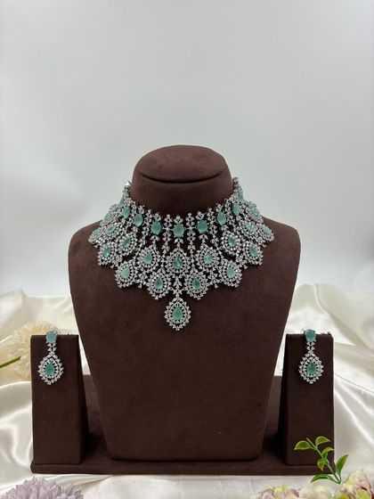 A heavy, silver-plated AD necklace set with a peacock-inspired feather design. This statement piece is available in blue, green, pink, and all-white.