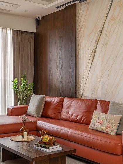 The living room features a bold orange leather sofa that infuses the space with energy. This is balanced by a sophisticated backdrop of book-matched marble and rich wood paneling, creating a dynamic mix of textures.