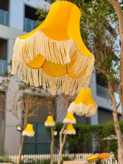 A bright and cheerful Haldi celebration with whimsical yellow lampshades hanging from the trees, perfectly capturing the sunny and happy spirit of the event.