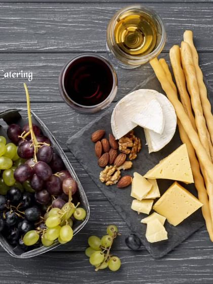 A sophisticated pairing of wine and cheese. This flat-lay shows a selection of cheeses, nuts, and breadsticks elegantly arranged on a slate board with glasses of red and white wine.