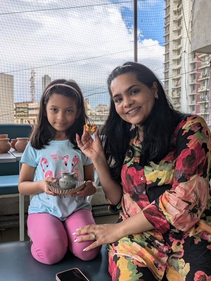 Proudly showing off their finished work. A mother and daughter smile with the small, painted bowl they created together, with the city skyline in the background.